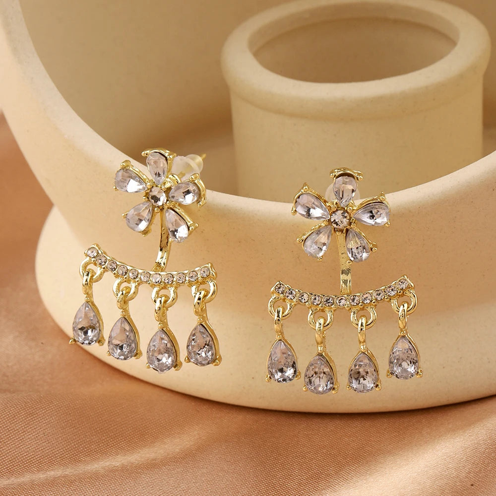 Gold flower and branch drop earrings displayed on fabric