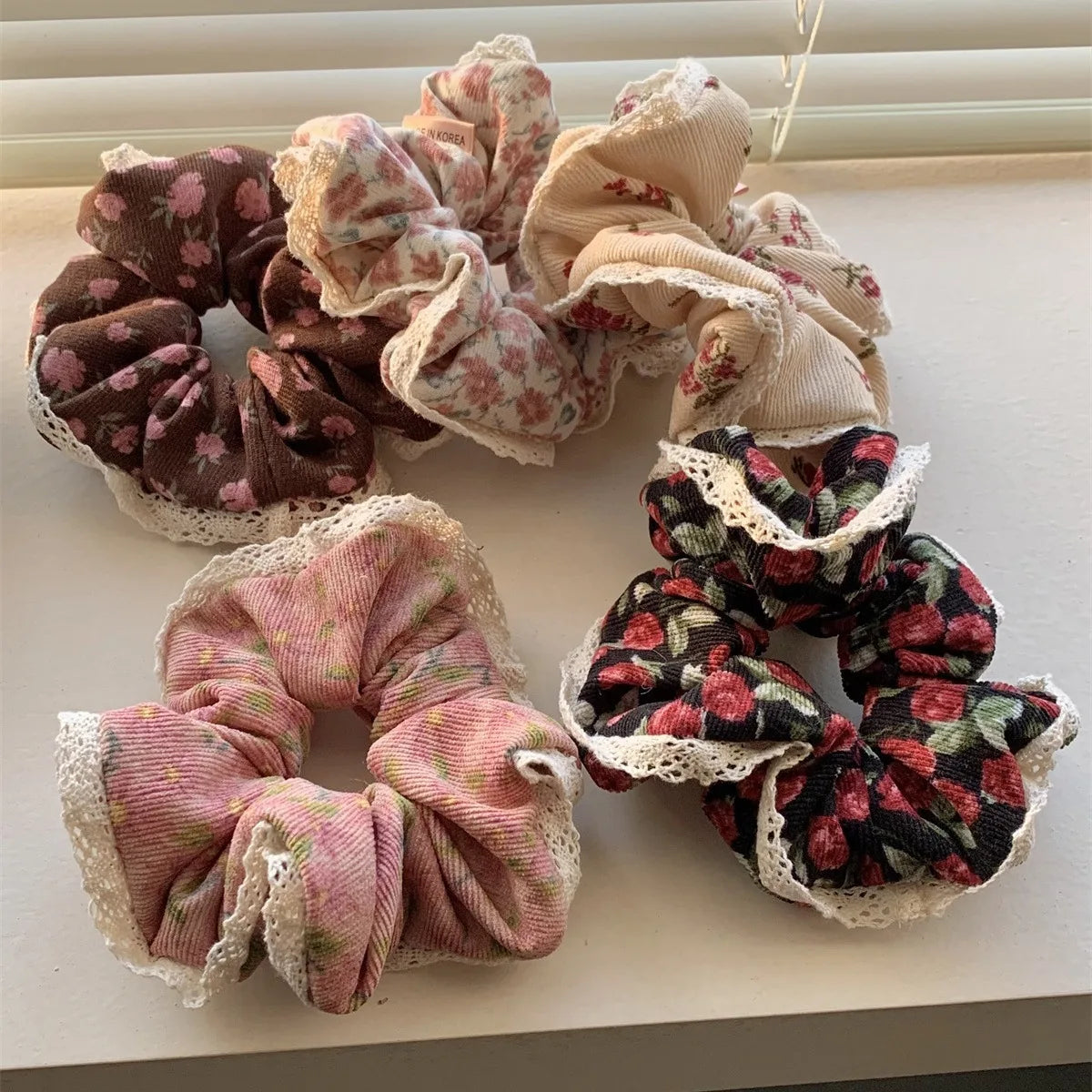 Assorted corduroy floral scrunchies in warm winter colors with lace borders.